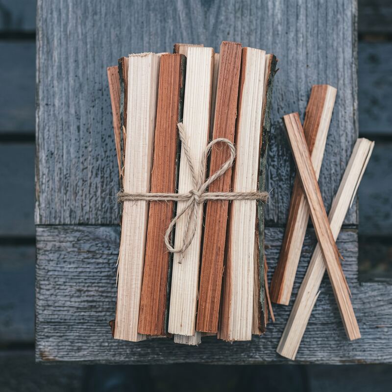 A bundle of dry split cedar and fir kindling tied with jute twine on a weathered grey plank